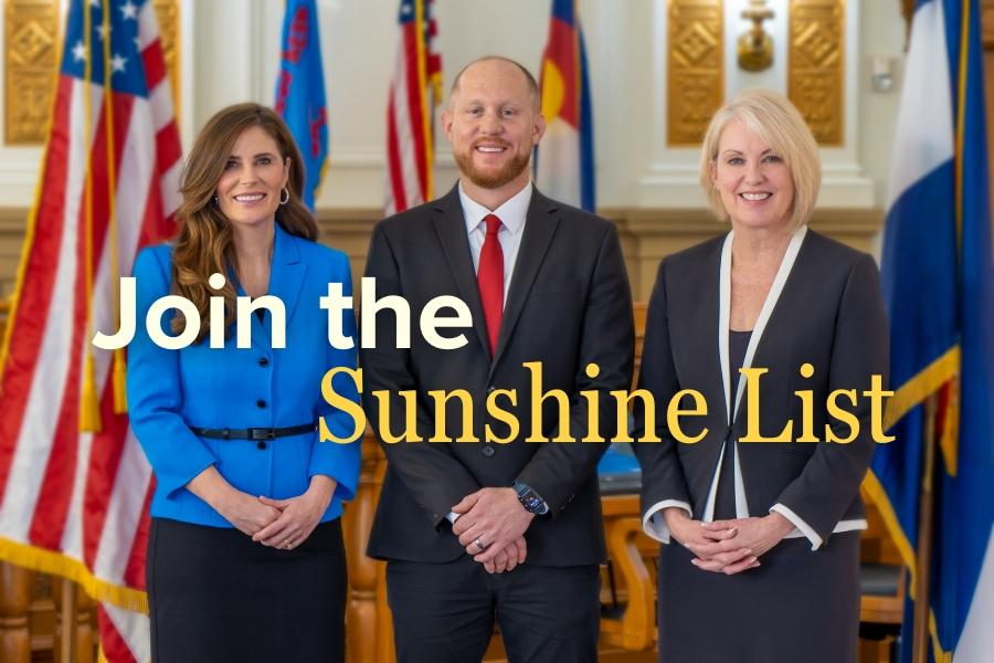 Two women and one man standing smiling wearing professional clothes. 