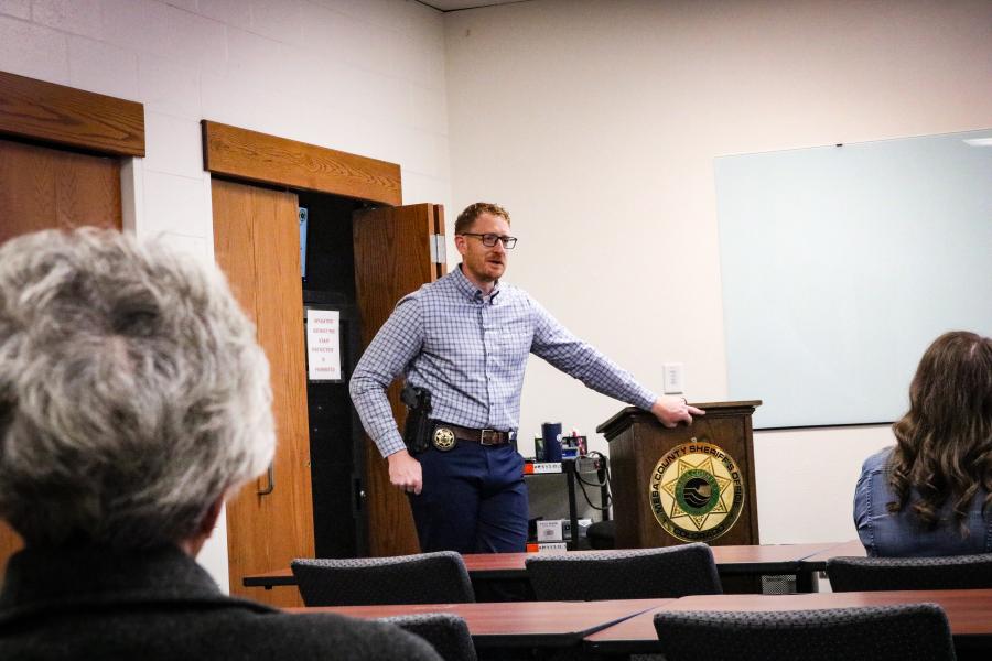 Sheriff's Office investigator speaking to a room of citizens, leaning on a podium with the agency logo on it